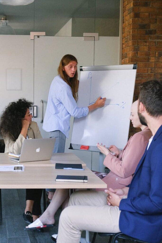 Pensive employee in formal clothes drawing graph on flipchart while explaining project to coworkers during seminar in workspace in daytime